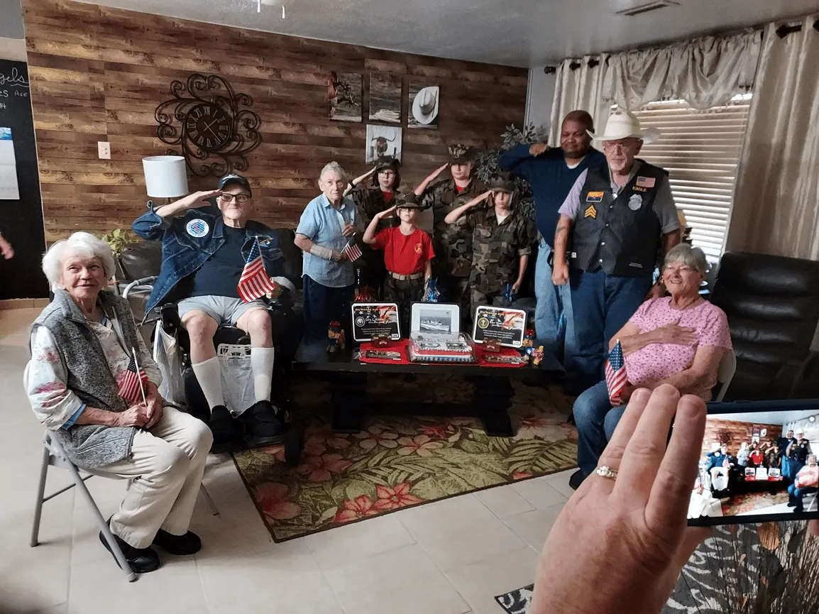 Group of people, including veterans and children in camouflage, saluting.