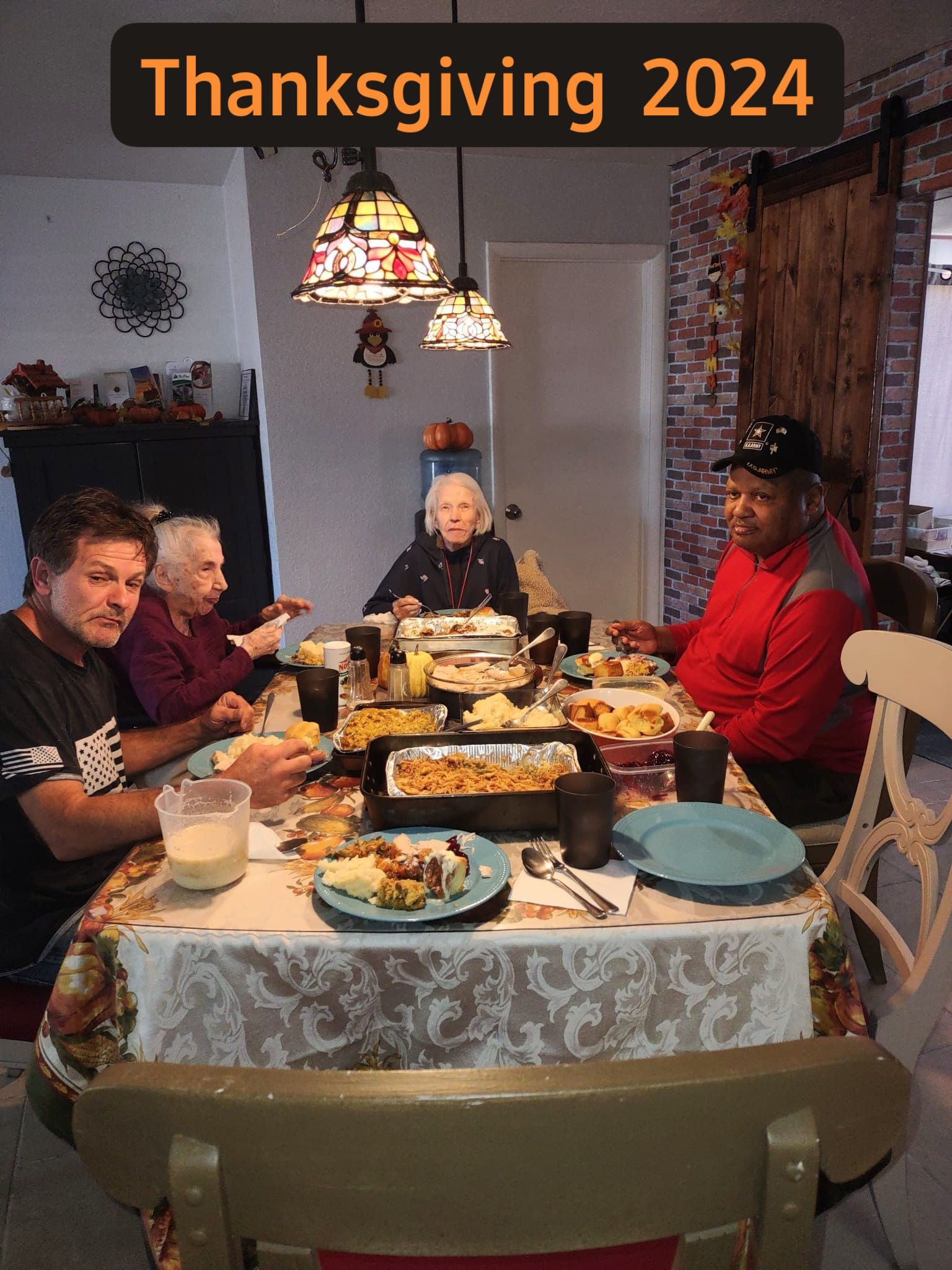 A Thanksgiving 2024 gathering: four people are seated around a decorated table laden with food, in a cozy home setting.