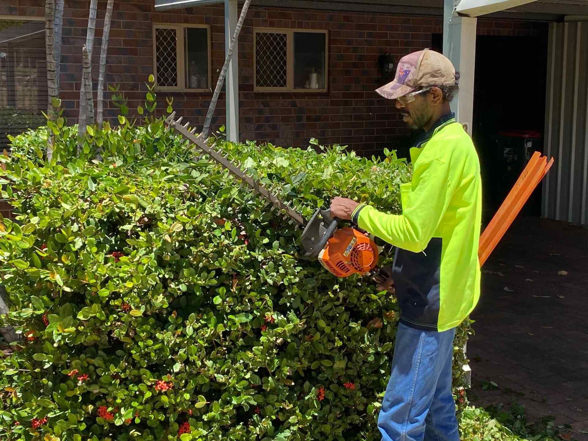 Man Trimming a Hedge With a Power Trimmer — Darrell's Mowing Services in Sunset, QLD