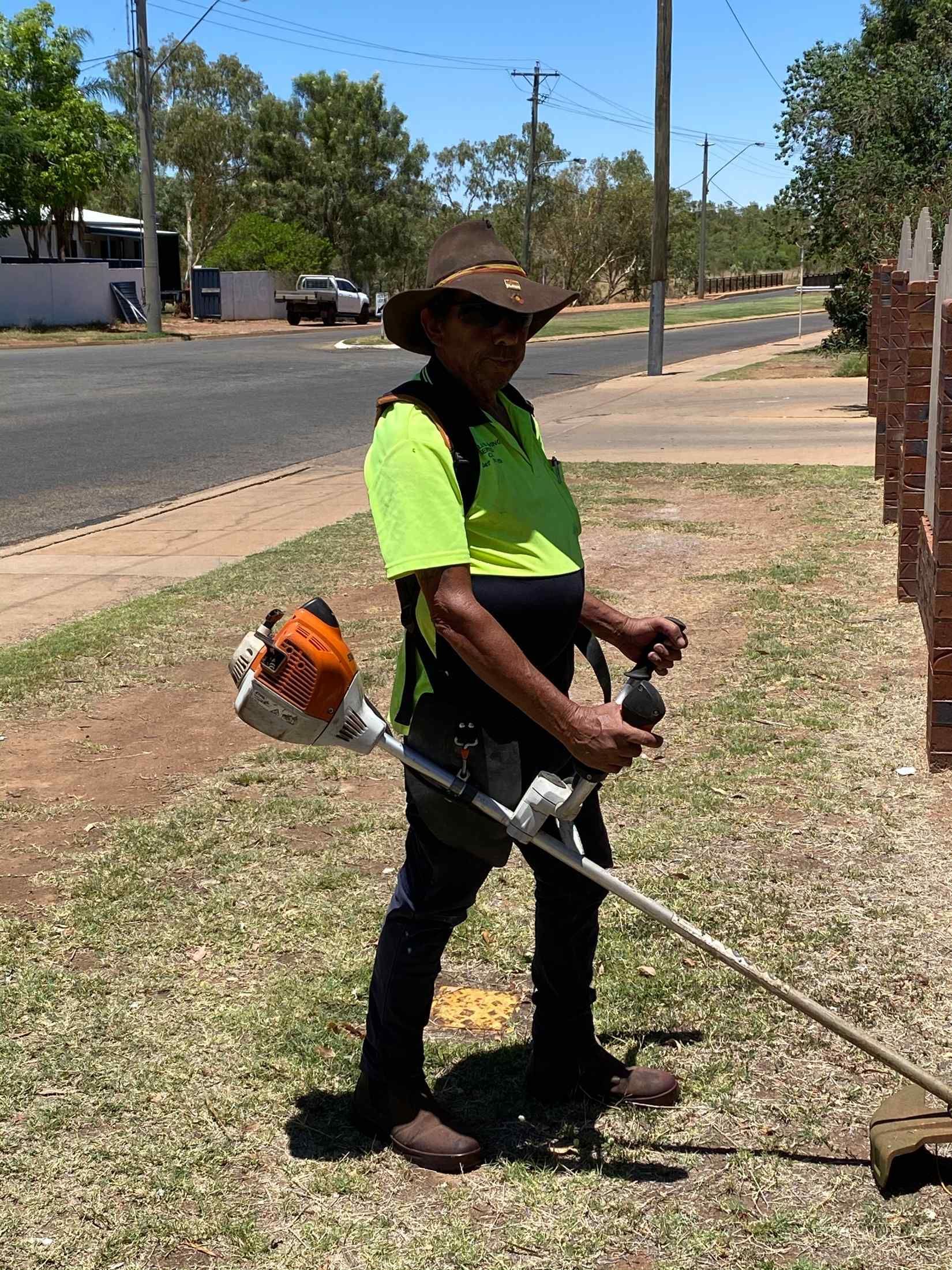 Person in Safety Vest Using a Weed Whacker on A Grassy Verge — Darrell's Mowing Services in Sunset, QLD