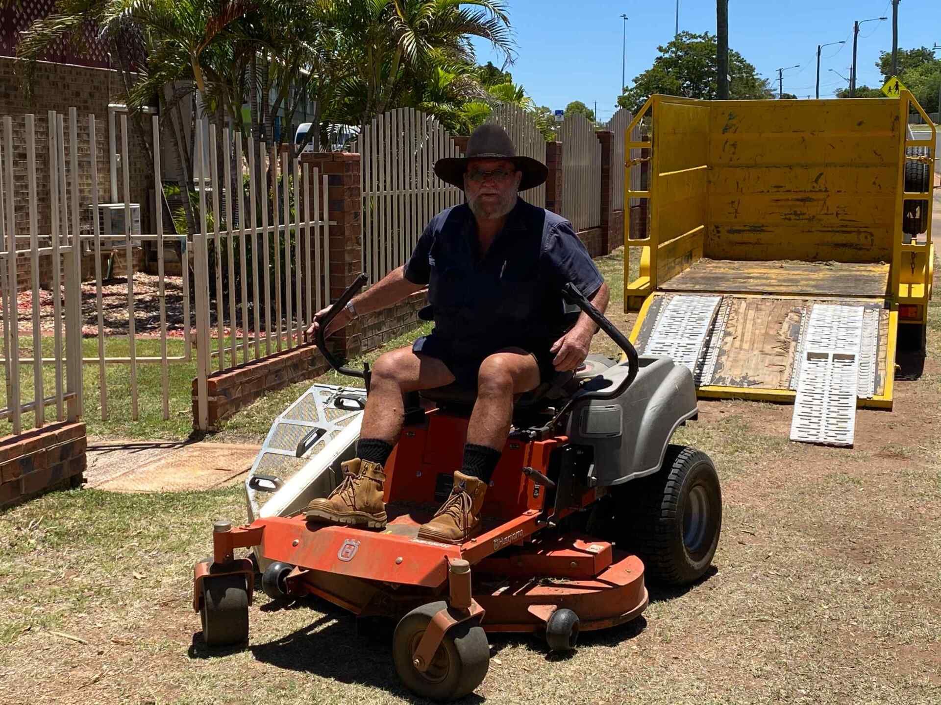 Man on Orange Riding Lawnmower Near Yellow Trailer; Residential Setting — Darrell's Mowing Services in Sunset, QLD