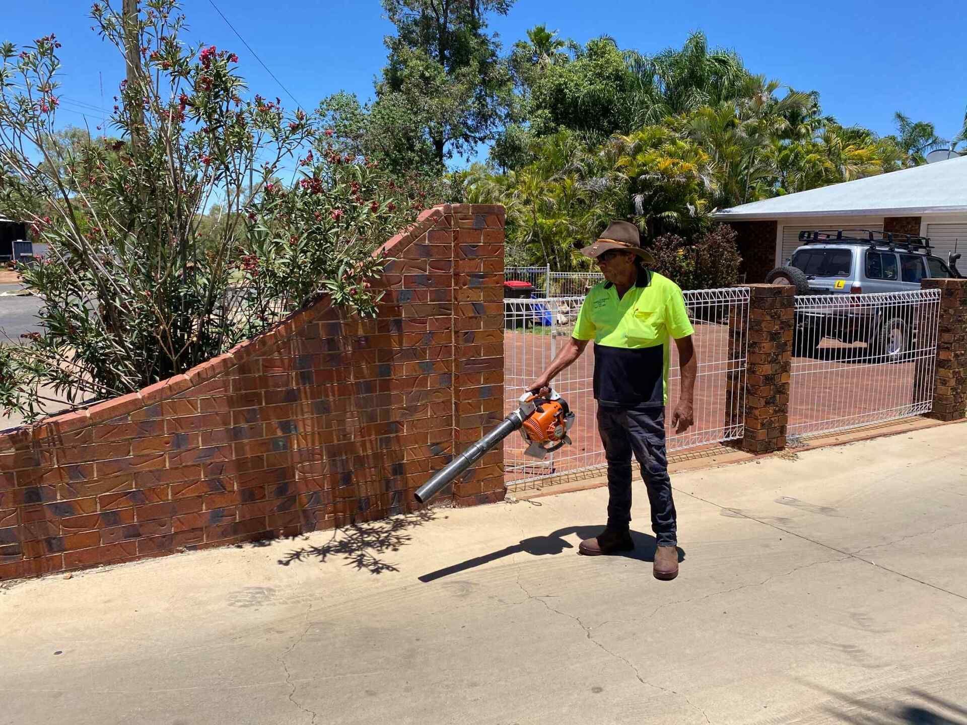 Man in a Yellow/blue Shirt Using a Leaf Blower on a Driveway — Darrell's Mowing Services in Sunset, QLD