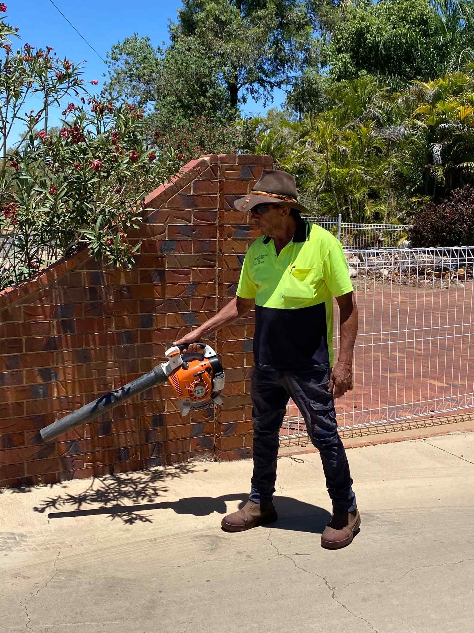 Man in Safety Vest Blowing Debris From a Paved — Darrell's Mowing Services in Sunset, QLD