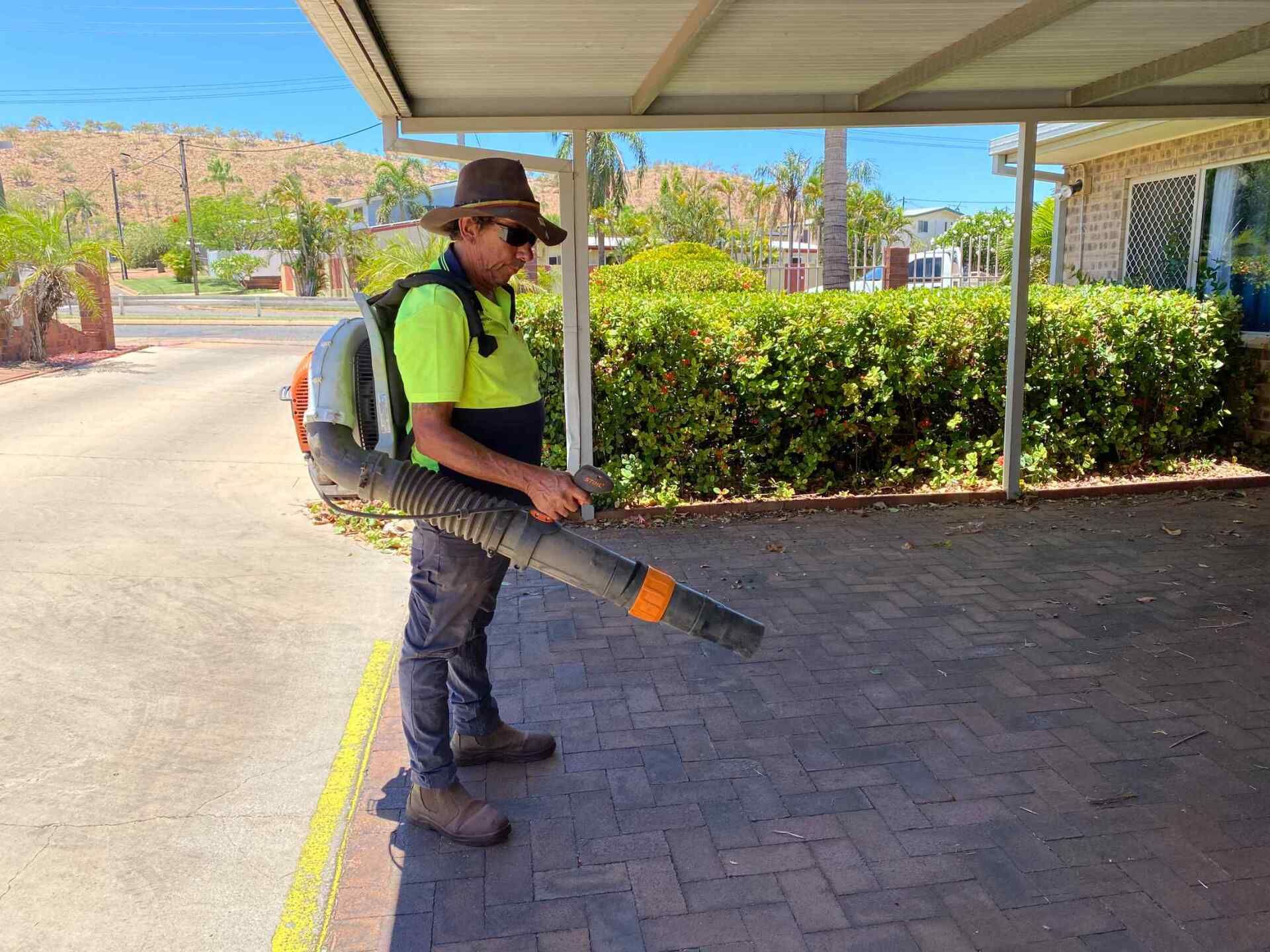 Man Using a Leaf Blower on a Brick Patio Under a Carport — Darrell's Mowing Services in Sunset, QLD