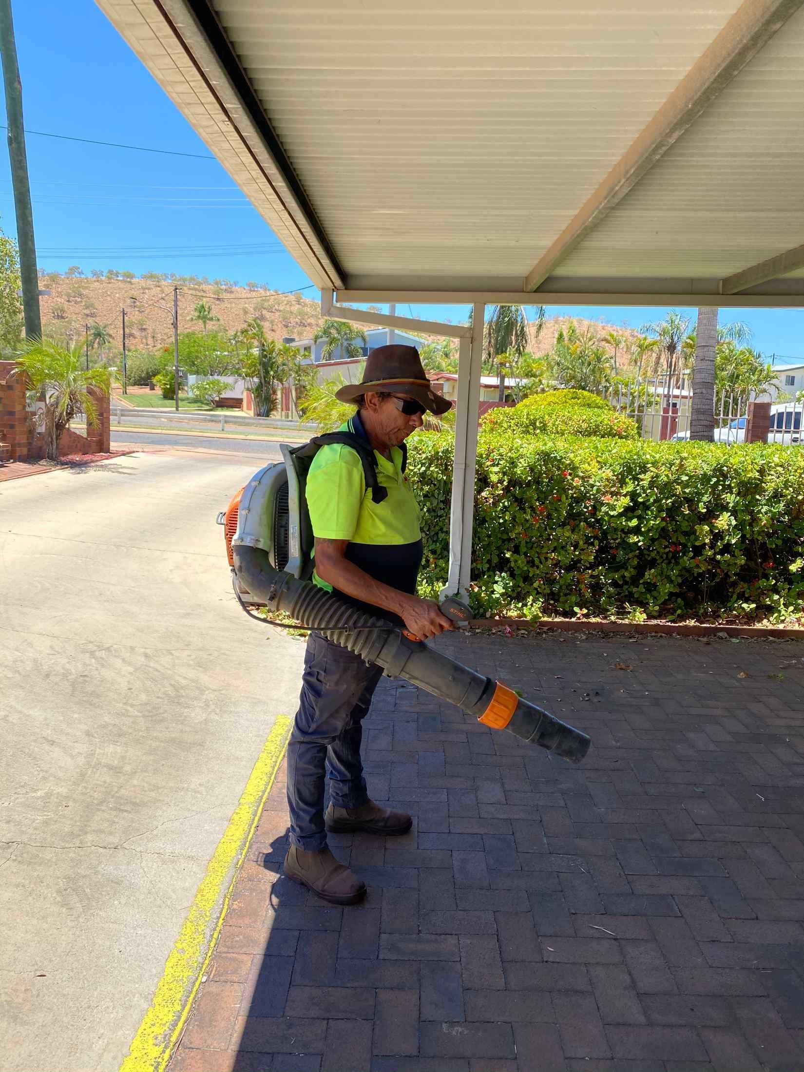 Man in a Hard Hat Using a Leaf Blower on a Brick Sidewalk — Darrell's Mowing Services in Sunset, QLD