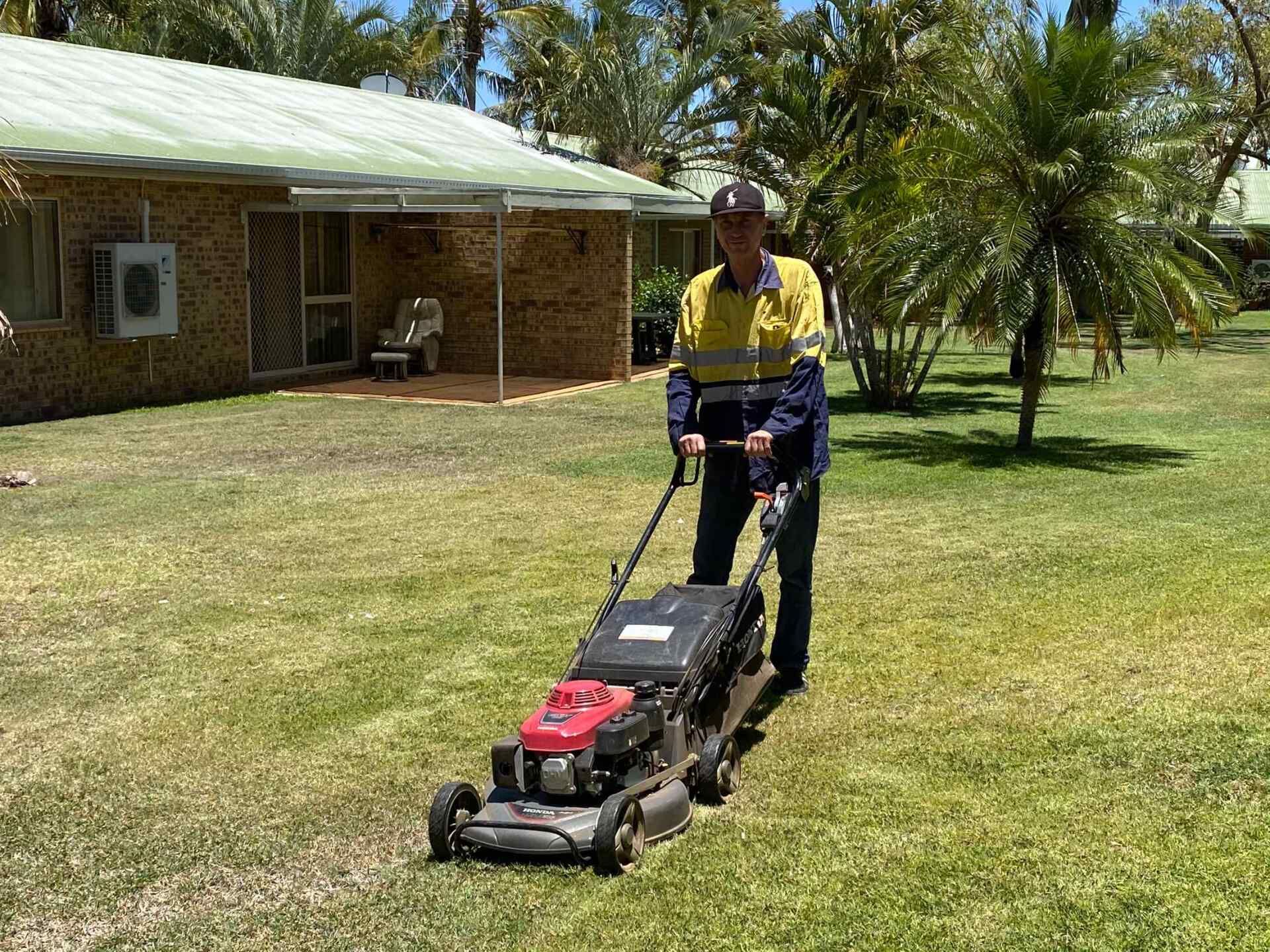Person in Workwear Mowing a Grassy Lawn With a Gas-powered Lawnmower — Darrell's Mowing Services in Sunset, QLD