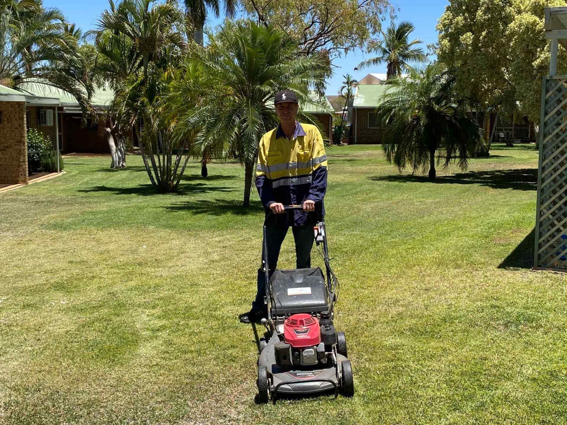 Person Mowing Lawn with A Red and Black Lawnmower — Darrell's Mowing Services in Sunset, QLD