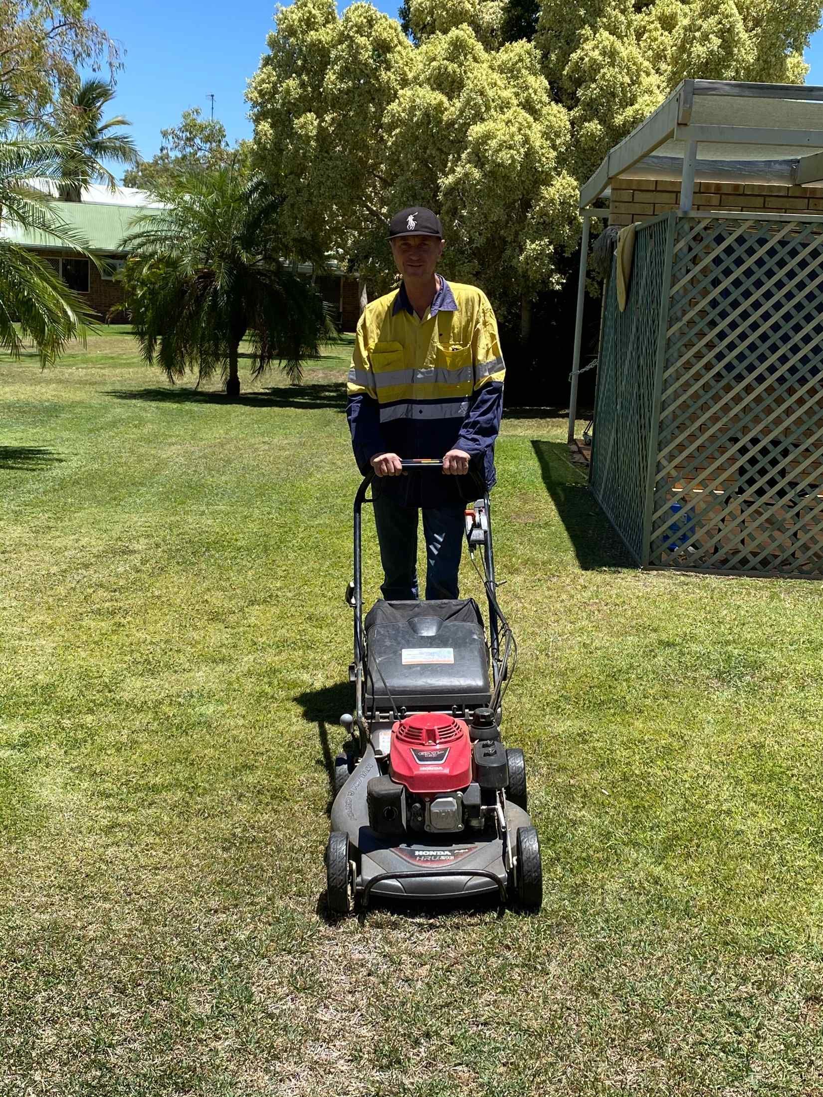 Person Mowing a Lawn With a Push Mower; Wearing a Safety Shirt — Darrell's Mowing Services in Sunset, QLD