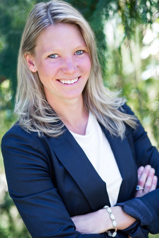 A woman in a suit and white shirt is smiling with her arms crossed.