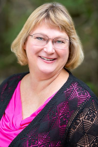 A woman wearing glasses and a pink shirt is smiling for the camera.