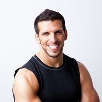 A man in a black tank top is smiling with his arms crossed.