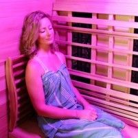 A woman is sitting in an infrared sauna with purple lights.