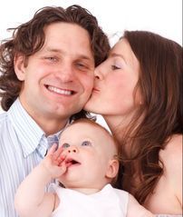 A woman is kissing a man on the cheek while holding a baby.