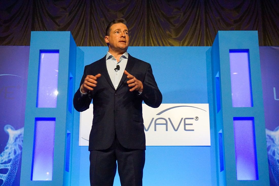 A man in a suit is giving a speech in front of a wave sign