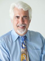 A man in a blue shirt and tie is smiling for the camera.