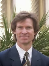 A man in a suit and tie is standing in front of a palm tree.