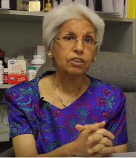 A woman in a purple shirt is sitting in front of a shelf full of pills