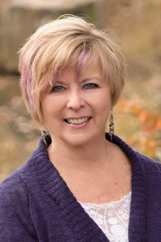 A woman wearing a purple sweater and earrings is smiling for the camera.