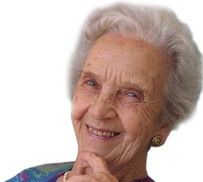 An elderly woman is smiling with her hand on her chin.