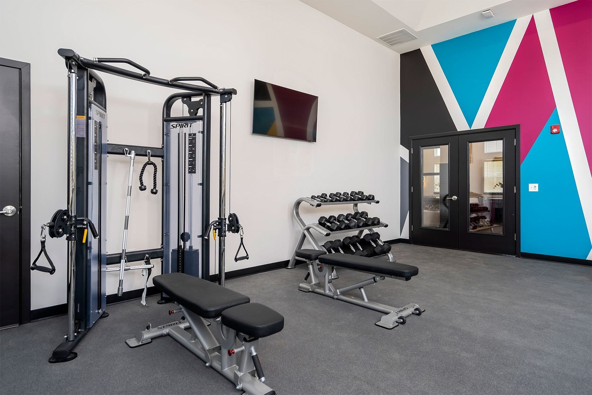 Fitness center with a variety of equipment including a squat rack, a leg press machine, and a bench with dumbbells.