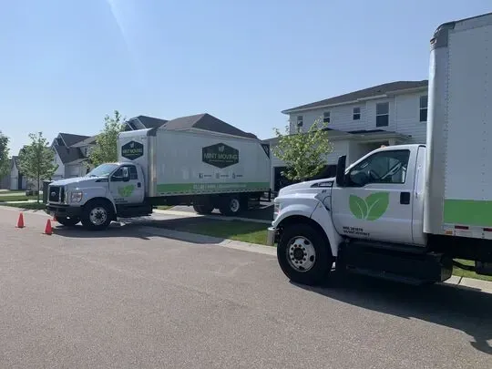 Two white trucks with green leaf logos parked on a residential street.