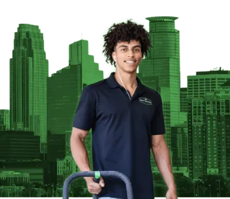 Man in black polo shirt holding equipment, with green city skyline in background.