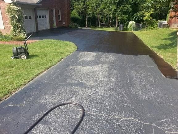 A driveway in the process of being resealed, with the darker fresh coating applied to the right side of the asphalt.