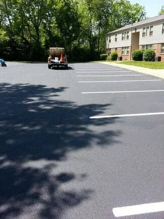 A paved parking lot with freshly painted white lines leading toward an apartment building and a truck in the distance.