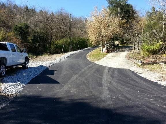 A white pickup truck parked on the left side of a newly paved asphalt driveway that branches off to a gravel path.