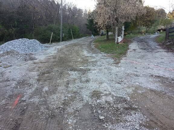 A dirt and gravel road splits into two paths near a pile of gravel and trees at dusk.