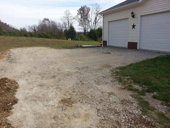 A gravel driveway leading to a two-car garage next to a grassy lawn on a sunny day.