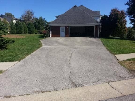A suburban house with a brick exterior and a paved driveway leading to a two-car garage on a sunny day.
