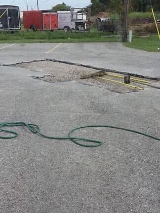 A large, rectangular asphalt patch in a parking lot, with a coiled green garden hose lying on the pavement in the foreground.