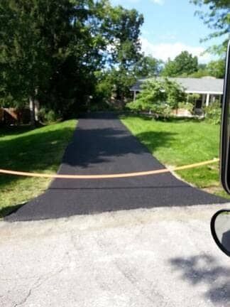 A freshly paved black asphalt driveway leads toward a house, blocked off by a thin orange safety line.