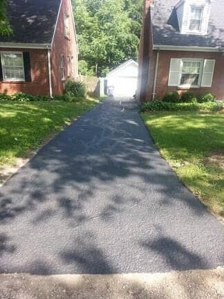 A freshly paved asphalt driveway sits between two brick houses, leading to a white garage in the distance.