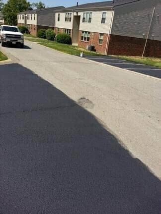 A paved driveway showing a stark color contrast between a freshly sealed, dark area and an older, light gray section.