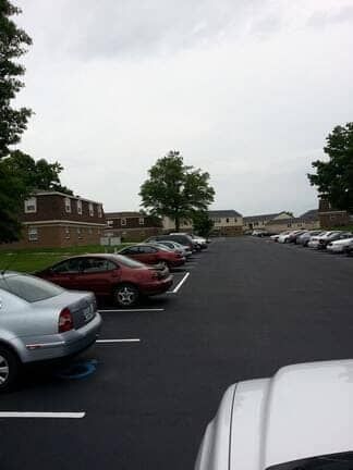 A parking lot on an overcast day, featuring several cars parked in spaces with apartment buildings in the background.