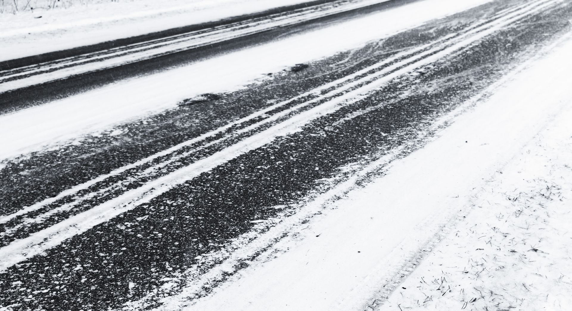 A snowy asphalt road with clear tire tracks carved through the center, leading into the distance. A snowy asphalt road with clear tire tracks carved through the center, leading into the distance.