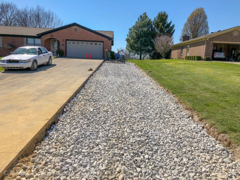A white sedan parked on a concrete driveway next to a newly installed gravel path leading toward residential houses.