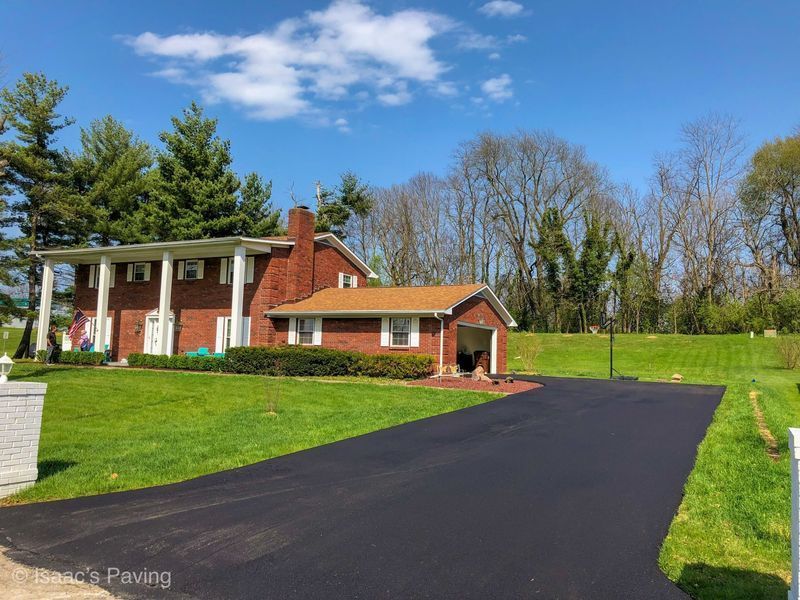 A large two-story brick home with a white columned porch and a freshly paved black asphalt driveway.