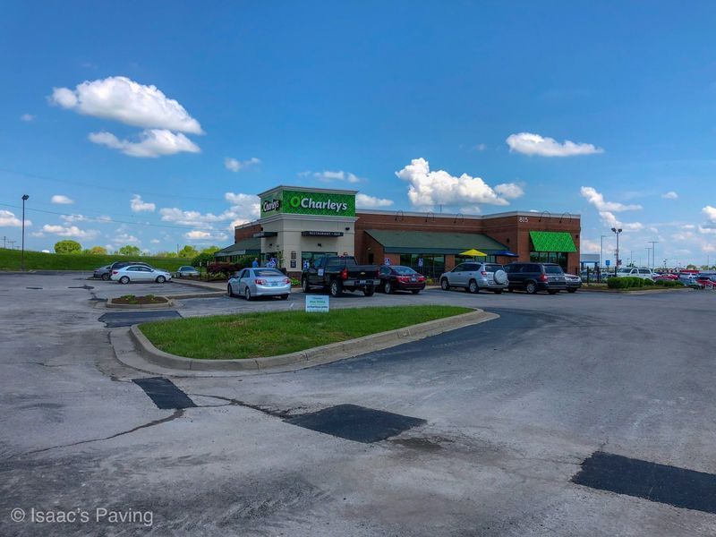 A commercial building with an O'Charley's sign and green awnings sits behind a large, paved parking lot under a blue sky.