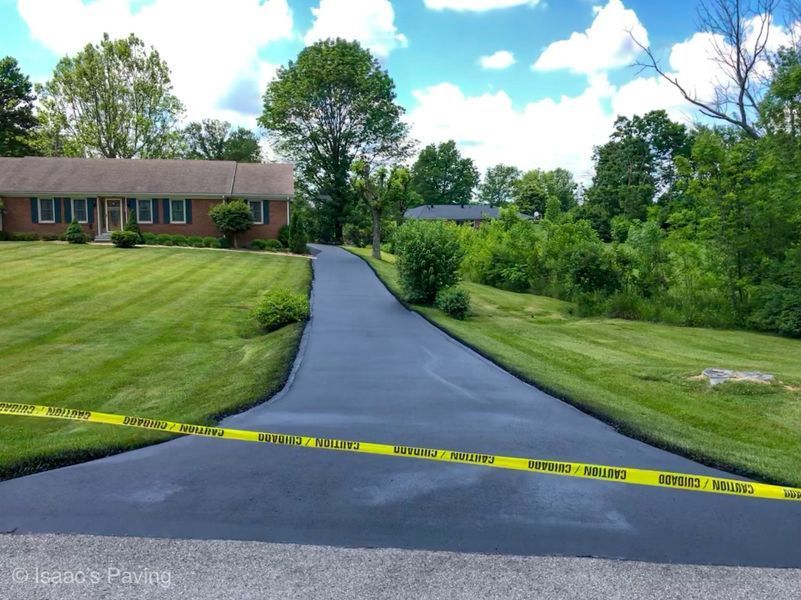 A newly paved, dark asphalt driveway leads to a suburban brick house, blocked off by yellow caution tape.