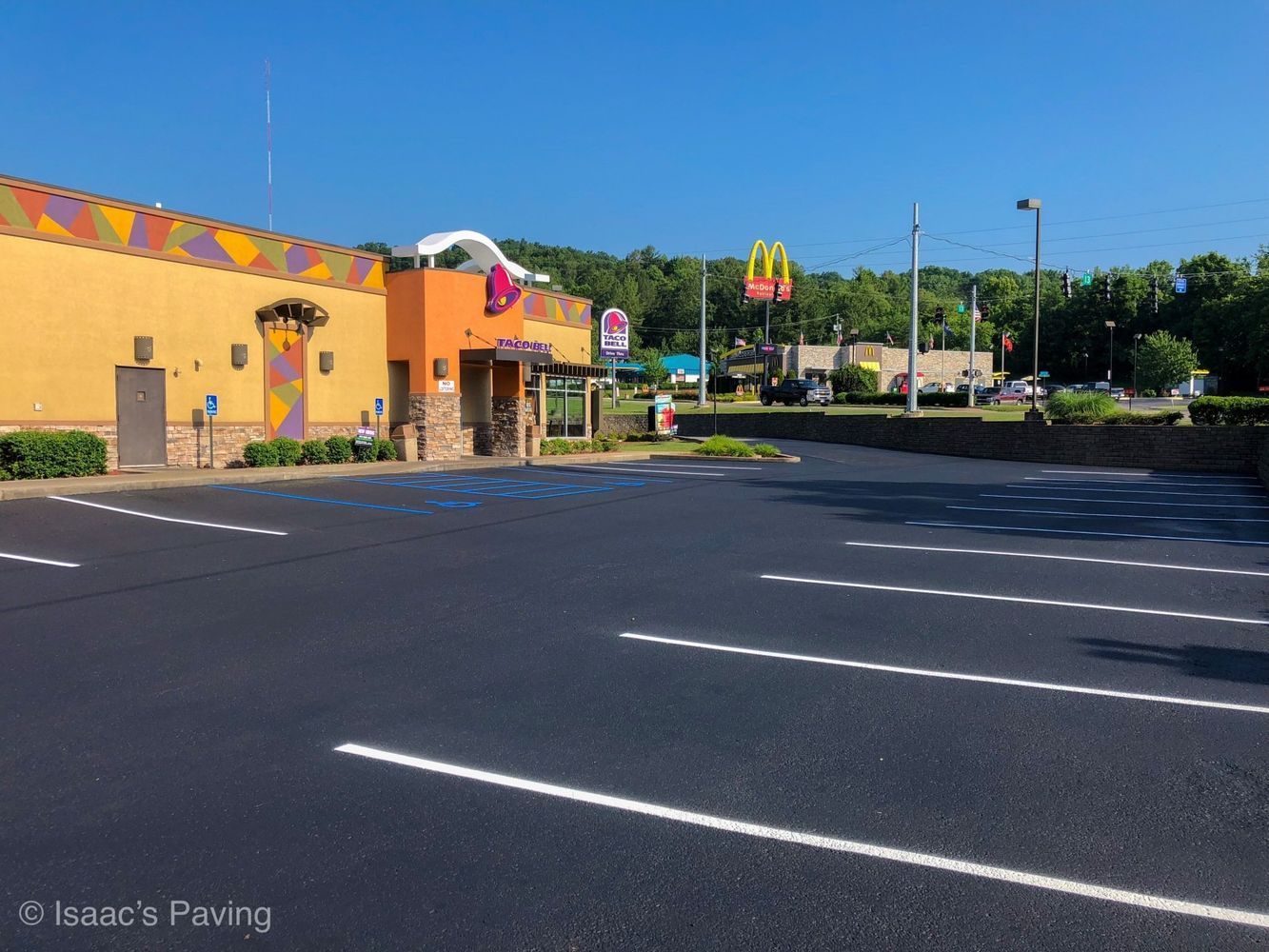 Freshly paved parking lot with marked handicap spaces in front of a Taco Bell, with a McDonald’s sign visible in the back.