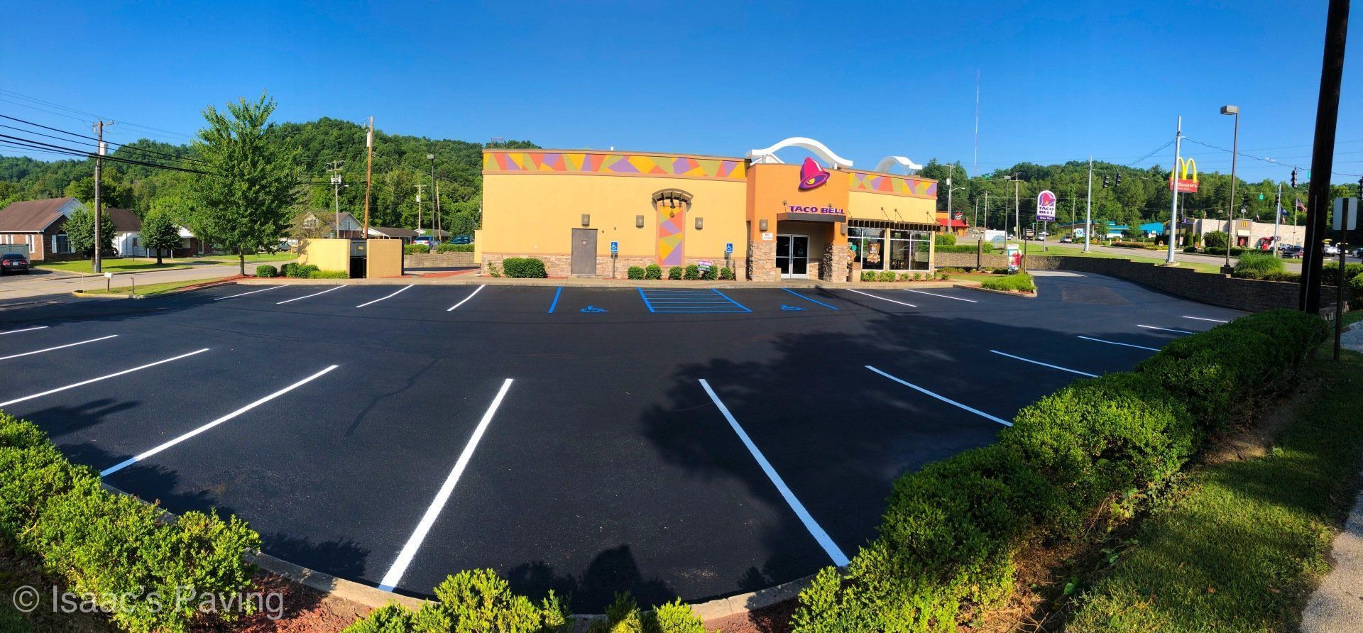 A wide-angle shot of a freshly paved Taco Bell parking lot with bright white painted lines under a clear blue sky.