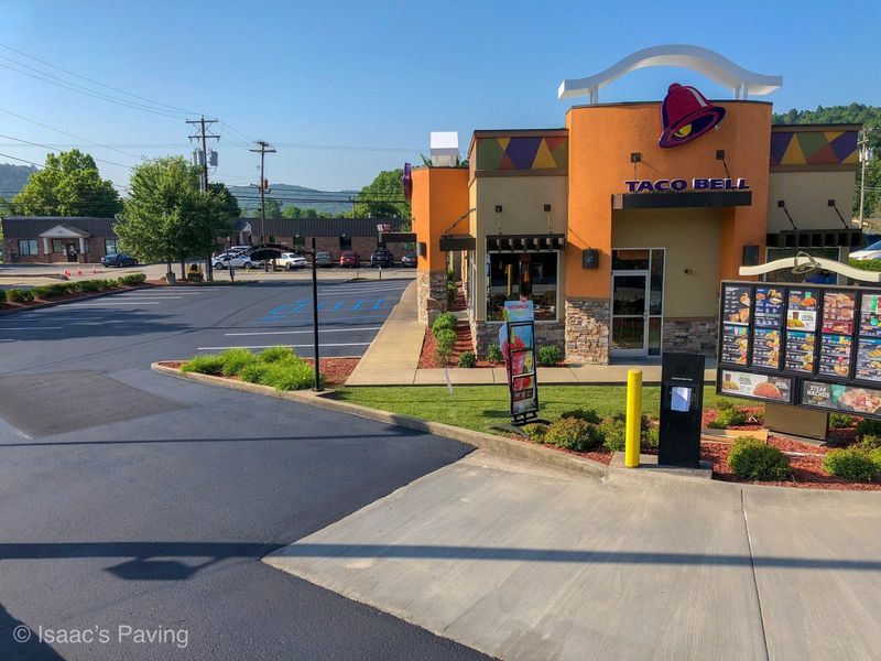 A Taco Bell restaurant with a freshly paved asphalt parking lot on a sunny day.