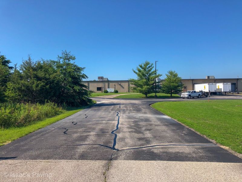 A paved path with a prominent crack leads toward a large commercial building with white trailers on a sunny, clear day.