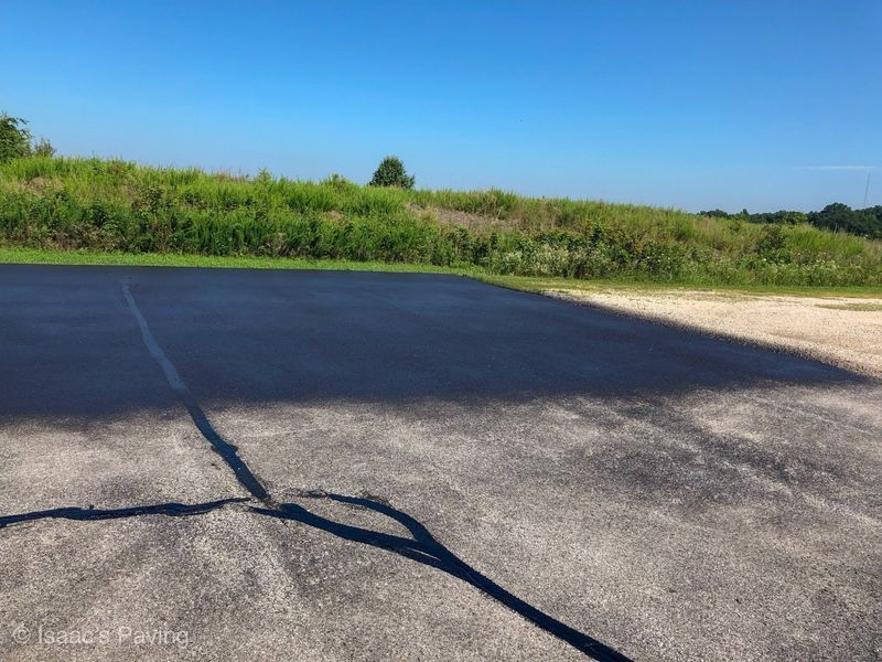 An asphalt lot showing a transition from old, weathered gray pavement to newly sealed, dark black surface.