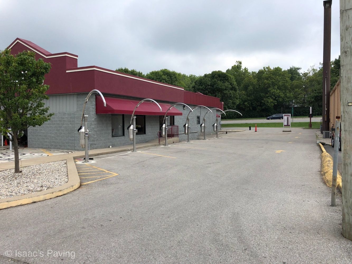 A paved lot with a red and gray building, featuring a row of silver vacuum stands under a red awning.