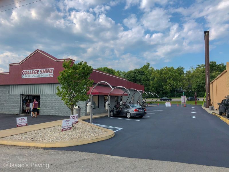 A freshly paved dark asphalt parking lot outside a College Shine car wash with a red facade and metal service awnings.