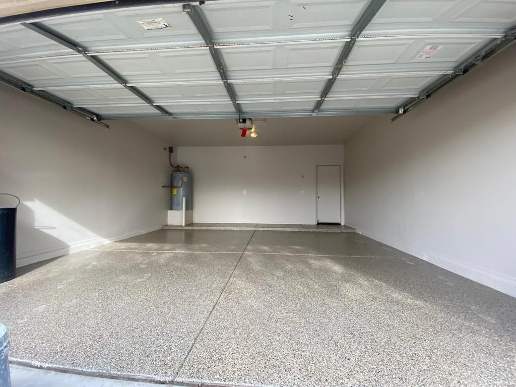 Empty garage with light-colored walls and epoxy floor. A water heater and overhead garage door track are visible.